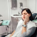 Woman holding her cheek in pain while visiting an emergency dentist in Fort Worth.