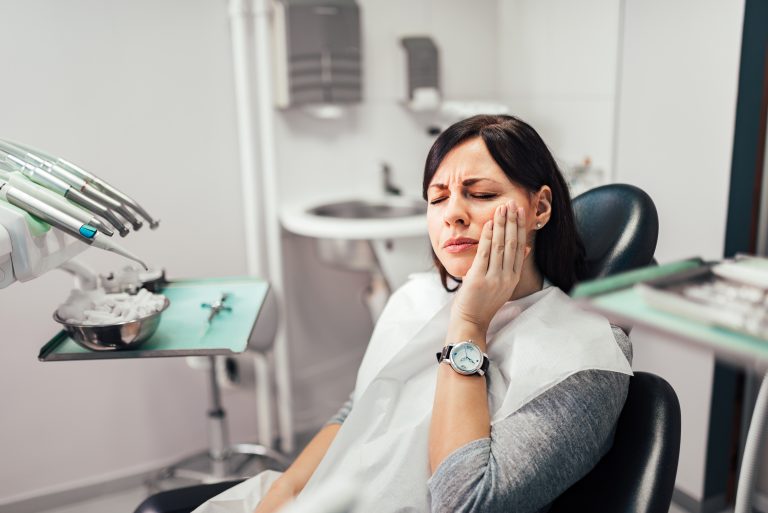 Woman holding her cheek in pain while visiting an emergency dentist in Fort Worth.